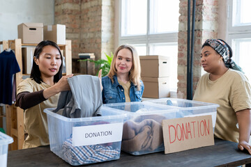 Wall Mural - Three multiracial females choosing donation clothes in plastic containers