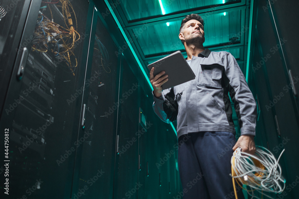 Low angle portrait of mature network engineer using digital tablet in server room during maintenance work in data center, copy space - obrazy, fototapety, plakaty 