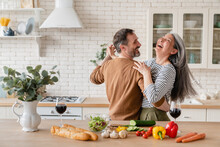 Happy Cheerful Middle-aged Mature Couple Family Parents Dancing Together In The Kitchen, Preparing Cooking Food Meal For Romantic Dinner, Spending Time Together. Active Seniors