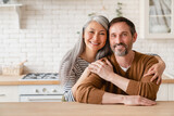 Fototapeta Panele - Cheerful happy mature middle-aged caucasian couple family parents husband and wife emracing hugging, spending time together in the kitchen at home, sharing love and care. Social distance concept