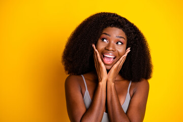 Photo of shocked dreamy lady hands cheeks open mouth look empty space wear top isolated yellow color background