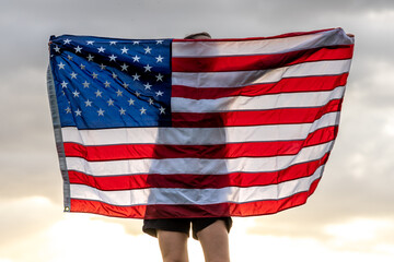 Back view of a girl with an American flag against the sky.