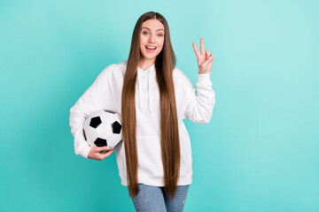 Poster - Photo of positive happy young woman hold hand football make v-sign isolated on pastel teal color background