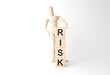 Wooden mannequin near tower of cubes with word risk on table against light background