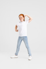 Wall Mural - Beautiful cute little red-headed girl in casual outfit having fun isolated on white studio background. Happy childhood concept. Sunny child