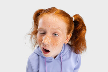 Wall Mural - Close-up funny girl with freckled face and red hair looking at camera isolated on white studio background. Happy childhood concept. Sunny child