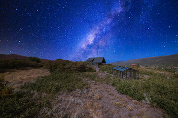 Building of a house with glass greenhouse in the middle of a shrubland under the vibrant night sky