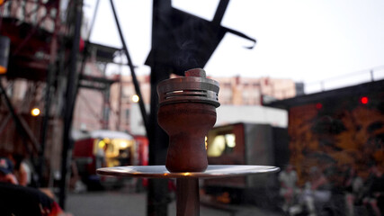 Hookah shisha smoke on city background. Close-up of a hookah bowl with charcoal. Hookah bar outside.