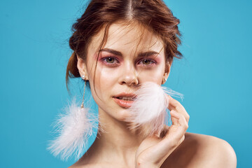 Wall Mural - woman with bright makeup on naked shoulders and fluffy earrings fashion blue background close-up