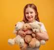 © Ievgen Skrypko - Beautiful girl child with three teddy bears isolated on yellow background with copyspace. Portrait of kid holding toys and smiling looking at the camera