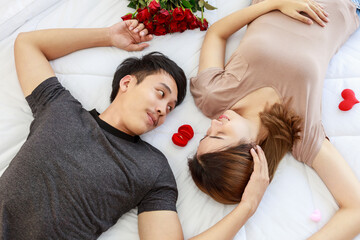 Couple, Love and Valentine's Day Concept. Portrait of two smiling asian man and woman looking on each other face and laying on bed in white blanket in bedroom with red engagement gold ring box