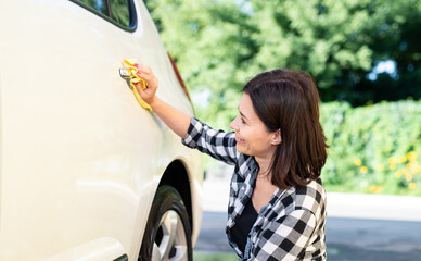 Wall Mural - Woman using microfiber rag for wiping car on nature background