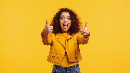 amazed young woman showing thumbs up isolated on yellow