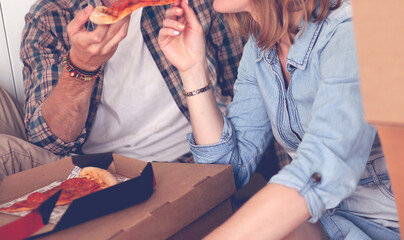 Young couple have a pizza lunch break on the floor after moving into a new home with boxes around them. Young couple