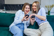 © Ivan - homosexual female couple on sofa look at smartphone and smile