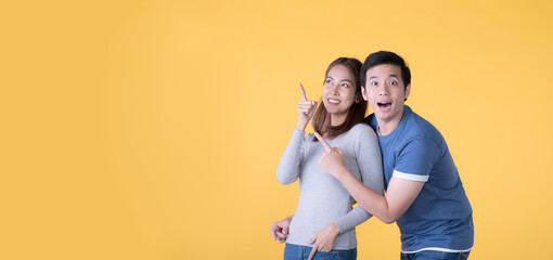 Excited Asian couple pointing fingers at empty copy space for text over yellow background