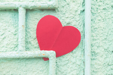 Red paper heart on a rustic green crumbling wall.the heart is pinned to an iron rod