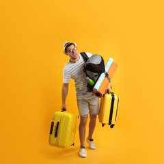 male tourist with travel backpack and suitcases on yellow background