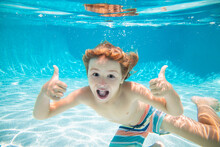 Happy Kid Boy Swim And Dive Underwater, Kid With Thumbs Up In Swimpool. Active Healthy Lifestyle, Water Sport Activity And Swimming Lessons On Summer Vacation With Child. Child Under Water.