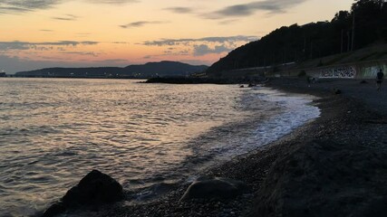 Wall Mural - Waves on the sea beach at sunset. Sunset with sea view. Amazing sunset over a tropical beach. A beautiful sunset against the background of mountains and a cloudy sky.