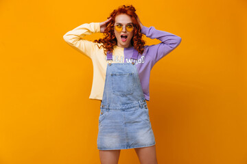 Wall Mural - Young girl in sundress and sweatshirt ruffles her curly hair against orange background