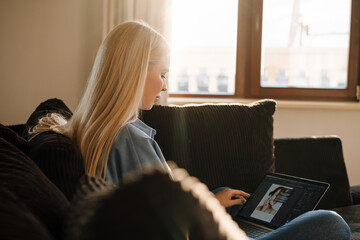 White blonde woman using laptop while sitting on sofa at home