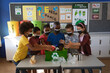 © Wavebreak Media - Group of diverse students wearing face masks putting recyclable plastic items in tray at school
