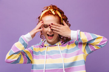 Wall Mural - Portrait of cheerful girl with yellow stylish hair bandage. Woman in striped hoodie poses on lilac background