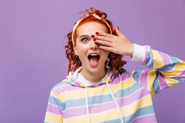 Wall Mural - Emotional girl covers eye with her hand and looks into camera against purple background