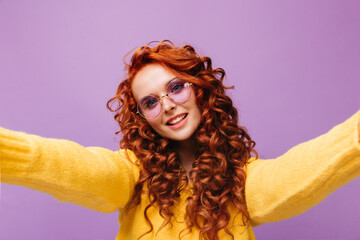 Sticker - Red-haired lady in round lilac glasses and bright sweater looks into camera and takes selfie on isolated background