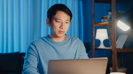 Asia freelance businessman focus working typing on laptop computer online remotely from company on desk in living room at home overtime at night, Work from home during COVID-19 pandemic concept.