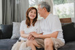 © tirachard - Asian senior couple relax at home. Asian Senior Chinese grandparents, husband and wife happy smile hug talking together while lying on sofa in living room at home concept.