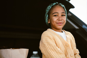 Black girl with pigtails smiling while sitting in car trunk