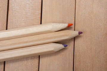 Top view of three colorful wooden pencils on a wooden table