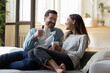 © fizkes - Calm relaxed couple hold cups rest on comfy sofa enjoy carefree talk while sit together on couch at modern living room. Homeowners family spend weekend at home, morning beverage, communication concept