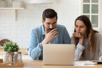 serious concerned married couple sit indoor looking at laptop read news, receive notification from b