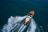 Fototapeta  - Classic Italian wooden boat fast moving aerial view. Top view of a wooden powerful motor boat. Luxurious wooden boat fast movement on dark water.
