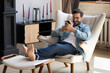 © fizkes - Handsome 30s single man relaxing on comfy armchair put feet on footstool holding in hands smartphone spend weekend alone in cozy cottage house. No stress, home owner, modern tech usage, fun concept