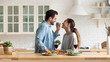 © fizkes - Caring husband feed his beloved mixed race wife, happy loving couple standing in modern domestic kitchen enjoy romantic dating with red wine and vegetarian salad. House-warming event, romance concept
