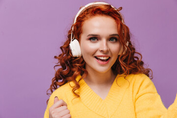 Wall Mural - Blue-eyed girl in yellow sweater listens to music with headphones and takes selfie