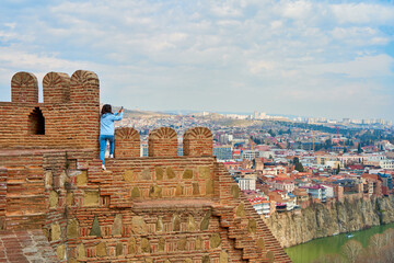 The girl enjoys the view and the silence while sitting on the wall of an ancient fortress overlooking the city