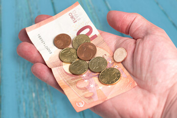 hand holding 10 Euro bill and small change against blue wooden table background