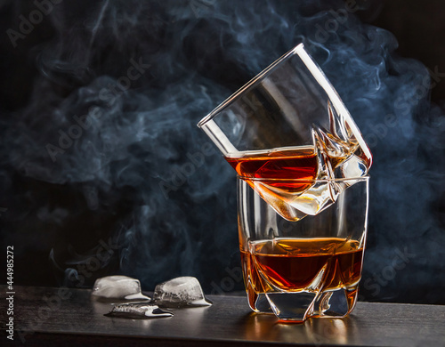 Two glasses of whiskey on a dark bar table, melting ice cubes from the left side, cigarette smoke at the background. Close up, copy space
