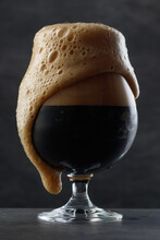 Detail Of Dark Beer With Overflowing Foam Head. Stream Of Dark Stout Pours Into A Beer Glass	