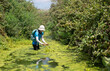 © A.Pushkin - Female hiker on a trail inside wadi Taninim in a hot summer day, Israel. Plenty of green vegetation growing on the banks of the stream and in water.