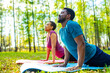 An attractive young woman and man doing yoga in green forest