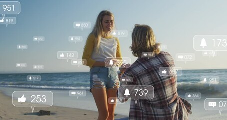 animation of social media icons over man proposing to his girlfriend on beach