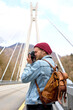 © alfa27 - Handsome hipster caucasian guy walking on bridge in urban area taking photo on camera, wearing denim jacket, looking at side, alone outdoors. travel, adventure, vacation concept