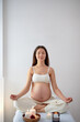 Pregnant asian woman relax doing yoga, sitting in lotus position in spa cabinet alone with candles, with eyes closed, keep calm. Health lifestyle pregnancy beauty, interior. Mom-to-be with naked tummy
