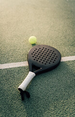 Padel racket and padel ball on a green court in the sunset